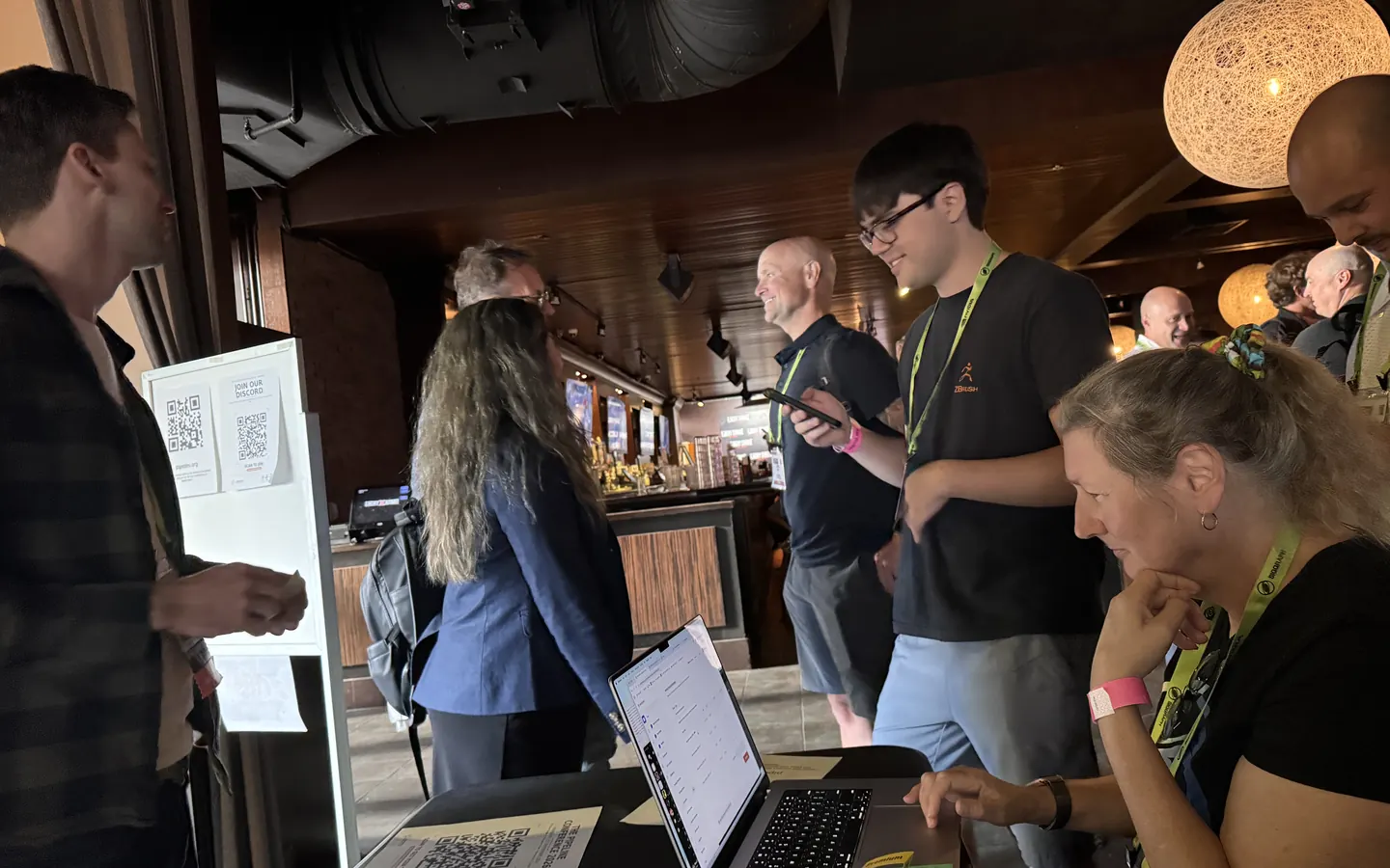 Pipeline engineers talking shop around a laptop at Beers of a Feather, the DPPA's SIGGRAPH 2026 meetup.